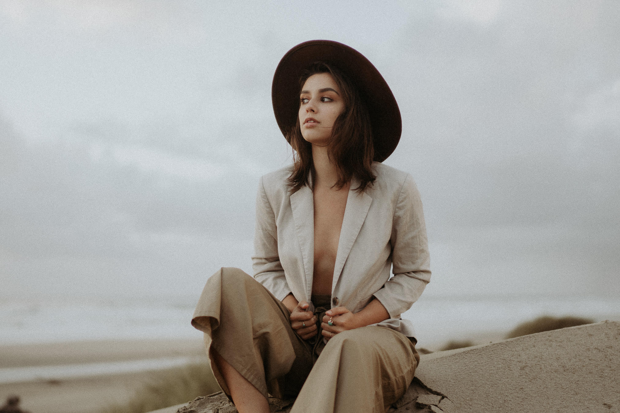 A woman in a hat sitting on a log beside the ocean