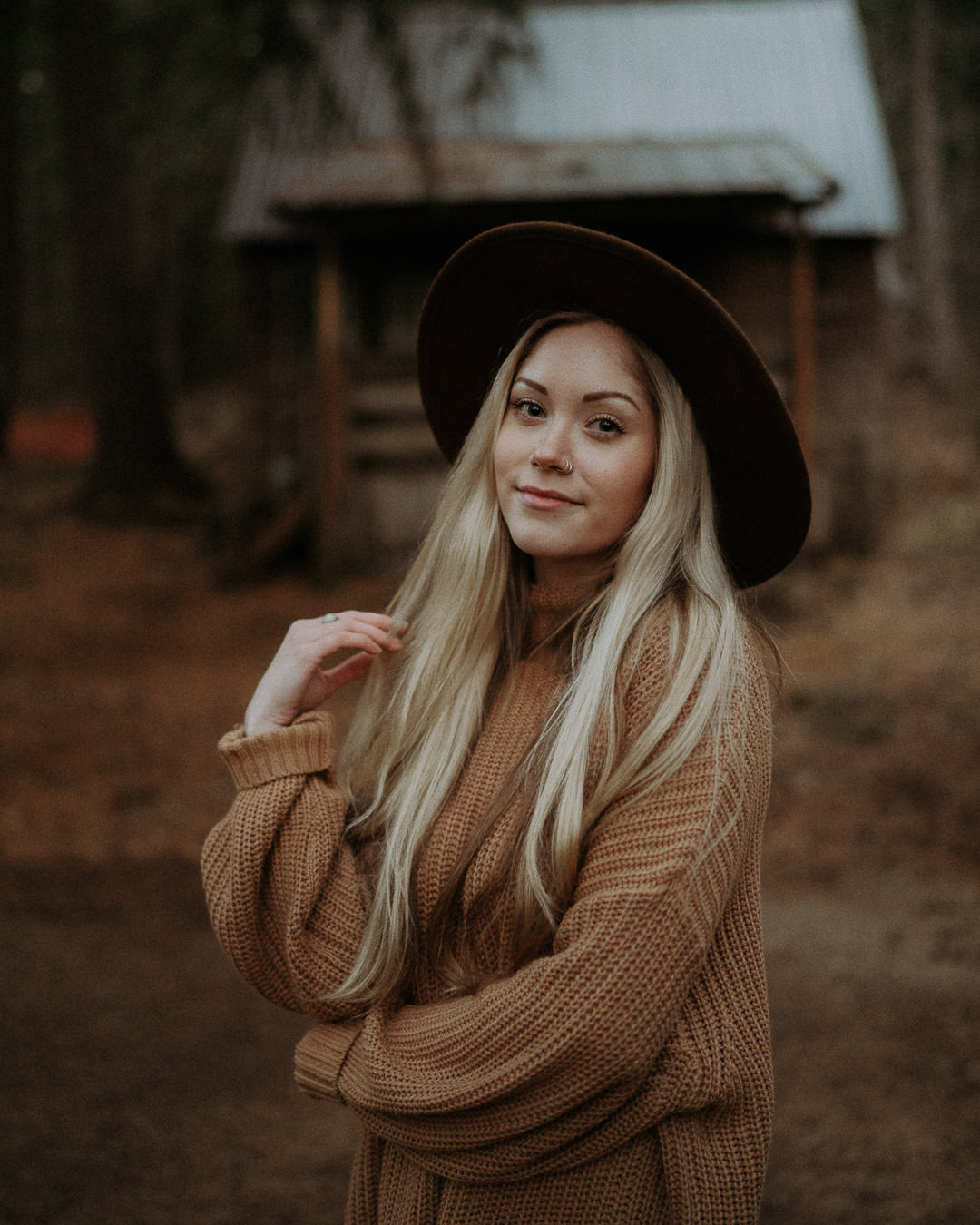 A woman in a brown hat standing outside a woodland cabin