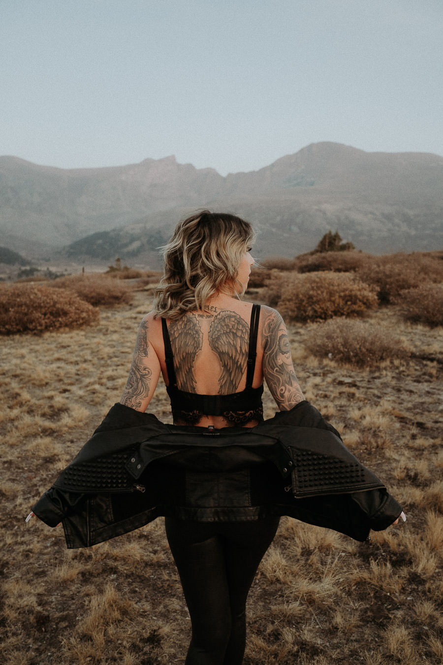 A woman turning away as her black jacket moves in a mountain meadow