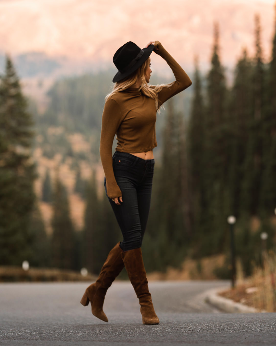 A woman in a hat moving along a mountain road in warm backlight