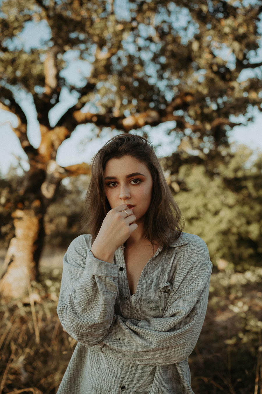 A woman in a denim jacket beneath a tree in evening light