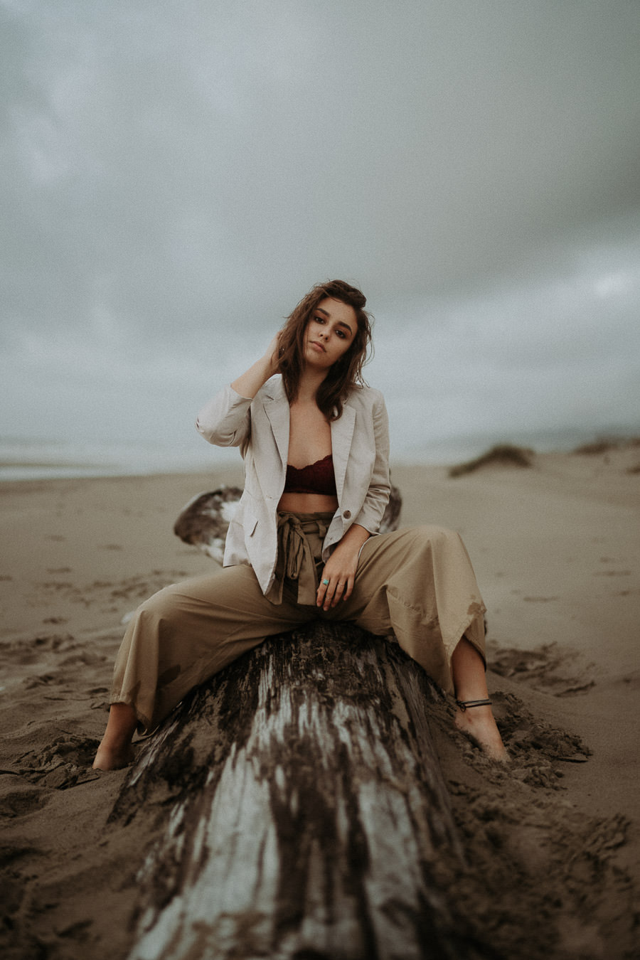 A woman in a light jacket sitting on a driftwood stump at the beach