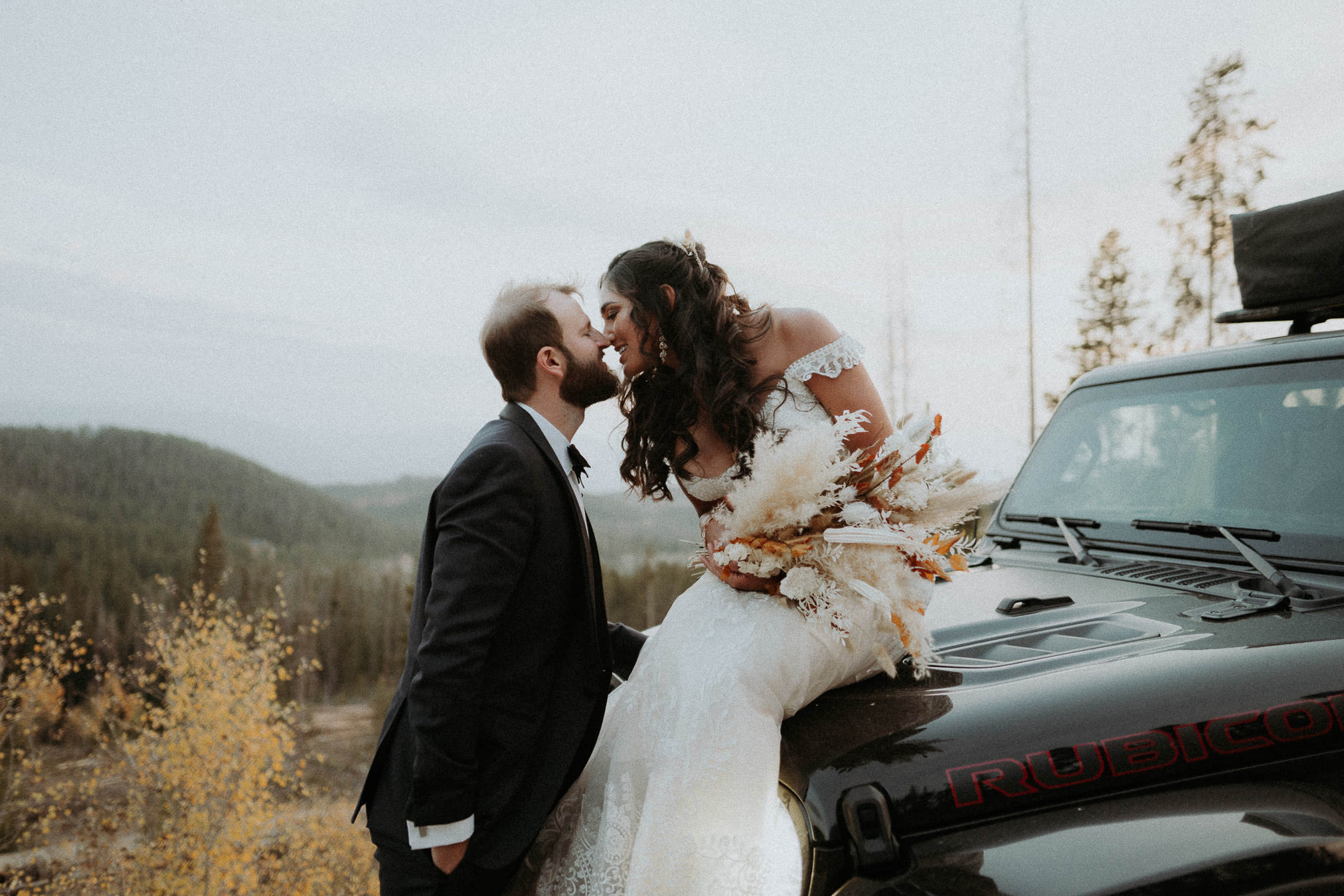Sam kissing Savanna as she sits on their Jeep beside a mountain road